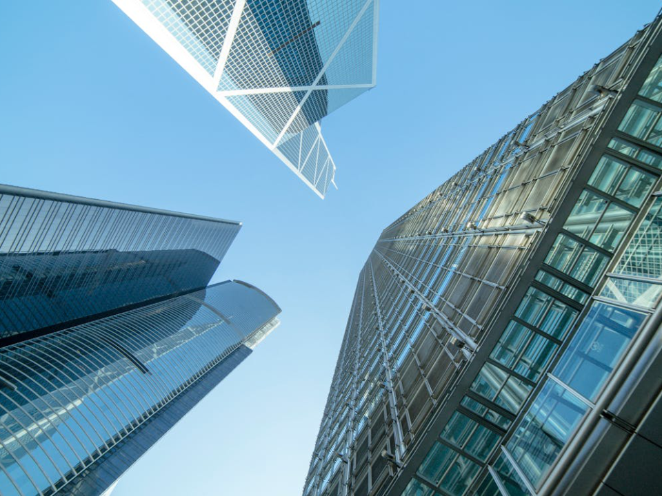 Low-angle view of modern skyscrapers reaching towards a clear blue sky with white clouds.
