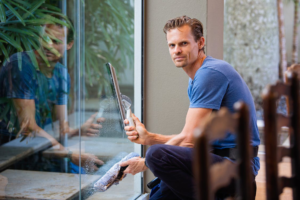 Man in a blue shirt cleaning windows with a squeegee.