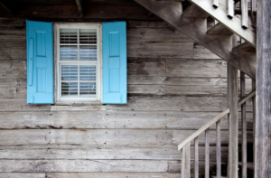 Brown wooden stair leading to a blue window on a house with siding.