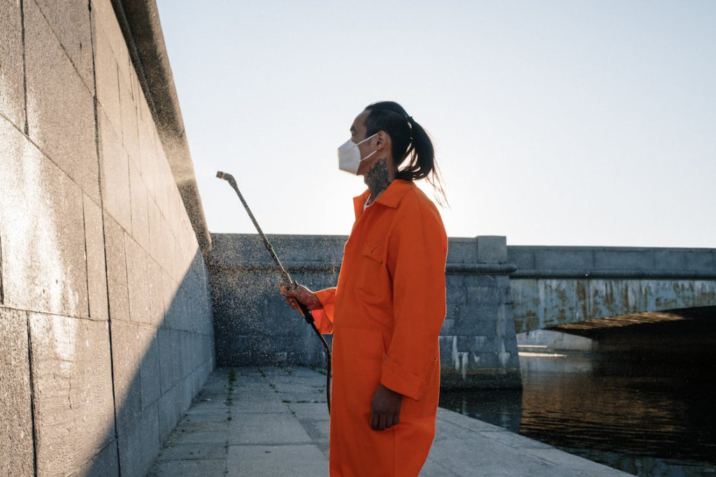 A man in an orange jumpsuit pressure washing a wall